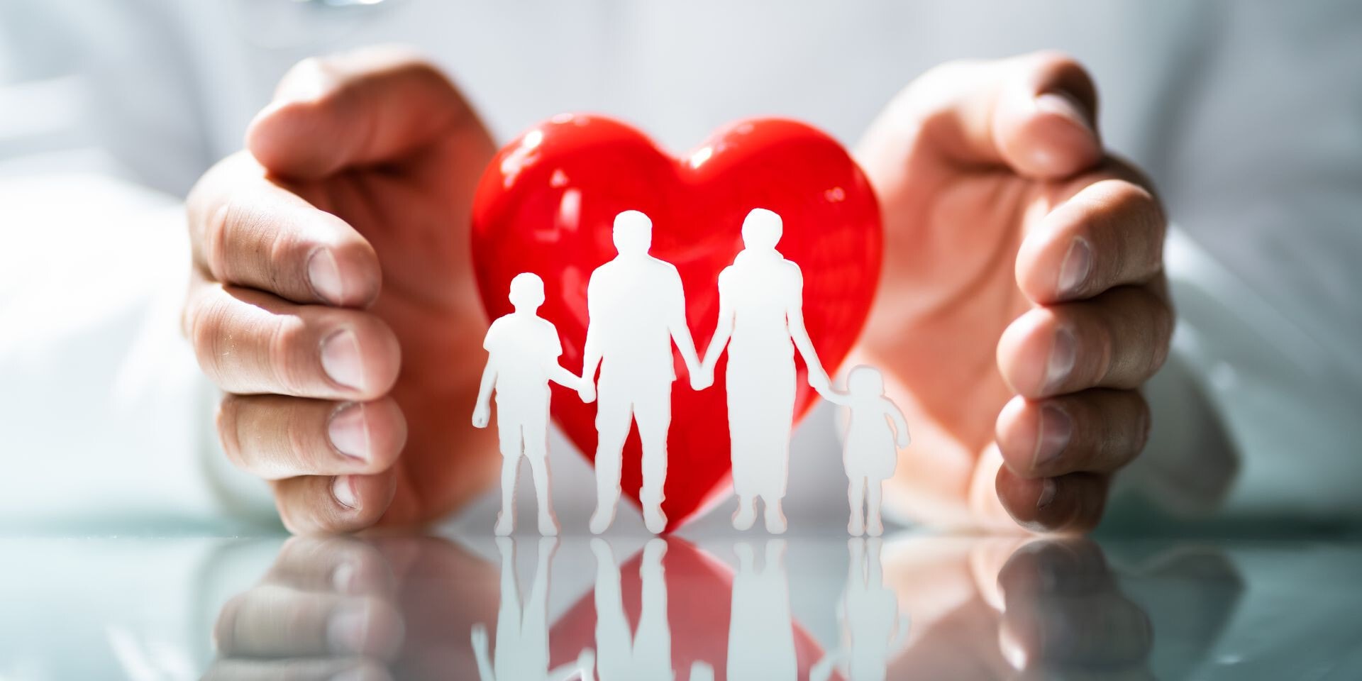 Twee handen die een groot rood hart en een wit silhouet van een familie beschermen.